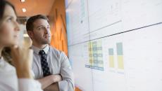 Two businesspeople looking at charts displayed on a large screen