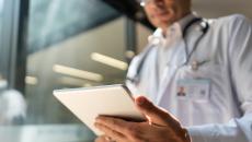 Healthcare provider wearing a lab coat and stethoscope while looking at a tablet