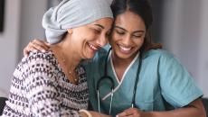 A healthcare provider with scrubs on sitting next to an oncology patient wearing a head scarf