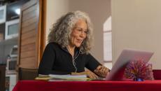 Person sitting at a table with a red table cloth on it while in a home looking at a computer