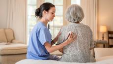 A provider listening to a patient's heartbeat in their home.