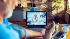 A patient talking to a doctor through a video chat on his computer while using a connected blood pressure device.