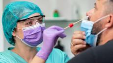 Female doctor in protective workwear taking nose swab test from middle aged man wearing protective face mask