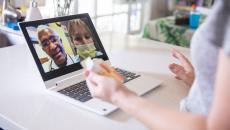 A close up of a woman holding a prescription while talking to two providers on her laptop