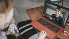 Person sitting down while looking at an orange and black laptop with a healthcare provider on the screen