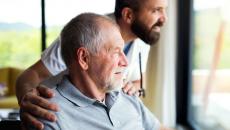 A person in a wheelchair and a healthcare provider standing beside them looking out a window