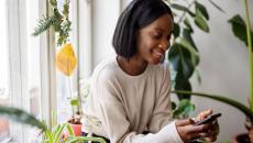 Person sitting in a chair and surrounded by plants while looking at a phone