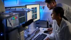 Two healthcare professionals, one sitting down and one standing up, looking at computer screens in a dark room