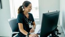 A healthcare provider with scrubs on and a stethoscope around their neck sitting at a desk while looking at a computer