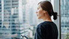 A person standing by a window using a smartphone. 